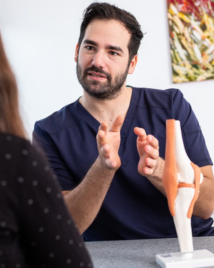 Dr. Patrik Shnawa erklärt einer Patientin Beschwerden am Kniemodell